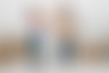 A woman hands a box to a man holding several boxes in a white room with stacked boxes labeled "Books." Both appear focused.