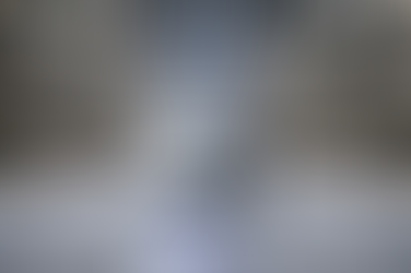 Autonomous white robot moves through a warehouse with tall shelves of boxes. The setting is industrial, with bright, even lighting.