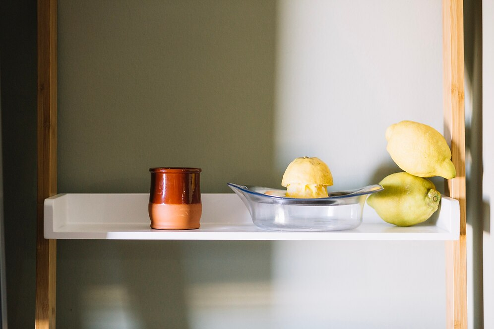 Shelf with a copper mug, a glass dish containing a juiced lemon, and two whole lemons. Background is grayish-green under natural light.