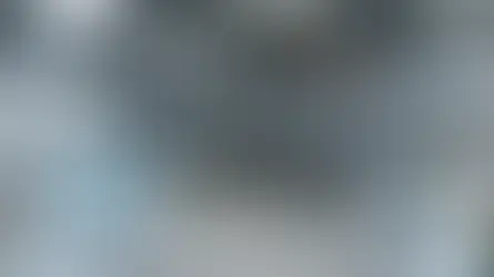 Industrial studio with mezzanine stacks of boxes, people working at a table below, and photography equipment set up. Bright, spacious atmosphere.