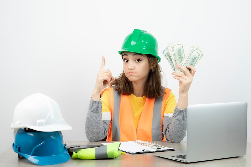 Woman in green hard hat and orange vest holds cash, pointing upward. Laptop, hard hats, and clipboard on table. Neutral background.