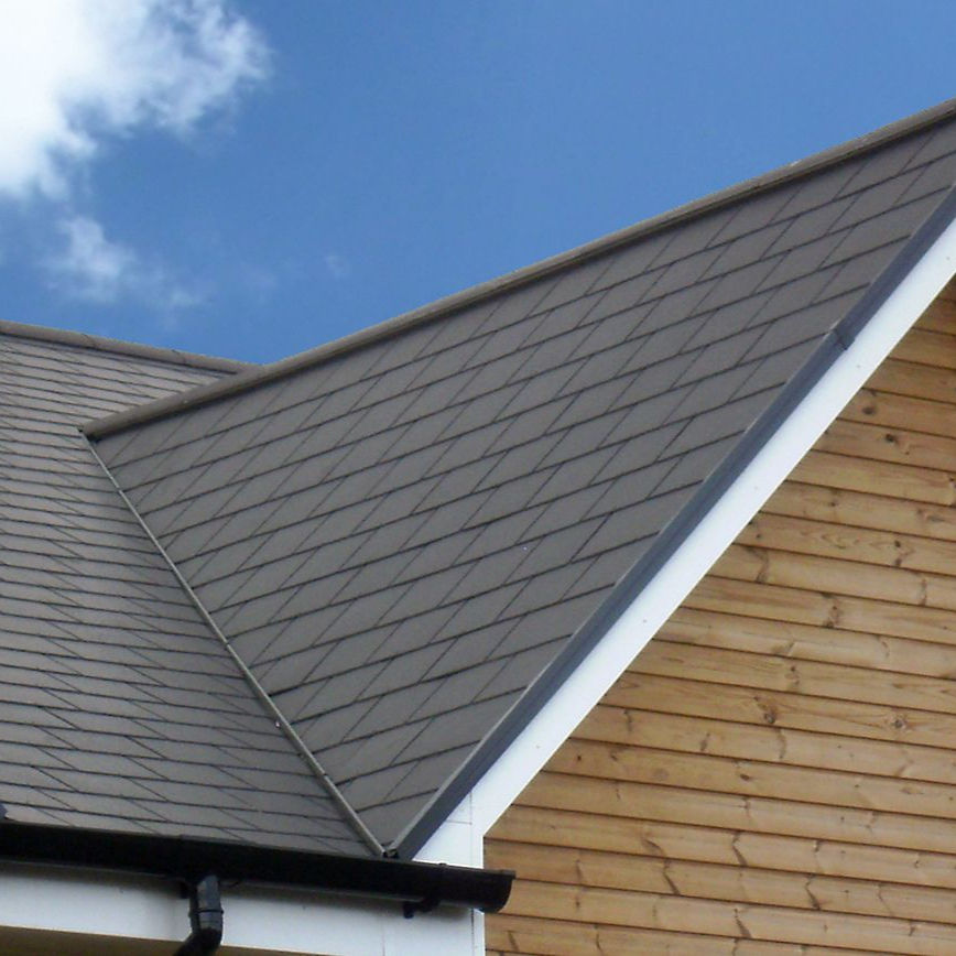 Gabled roof with gray shingles against a blue sky with few clouds. Wooden house siding visible below the roof. Calm and clear setting.