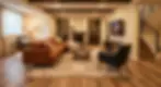 A cozy living room with a brown sofa, armchairs, and a wooden table on a beige rug. Fireplace, bookshelves, and TV on cream walls. Warm lighting.