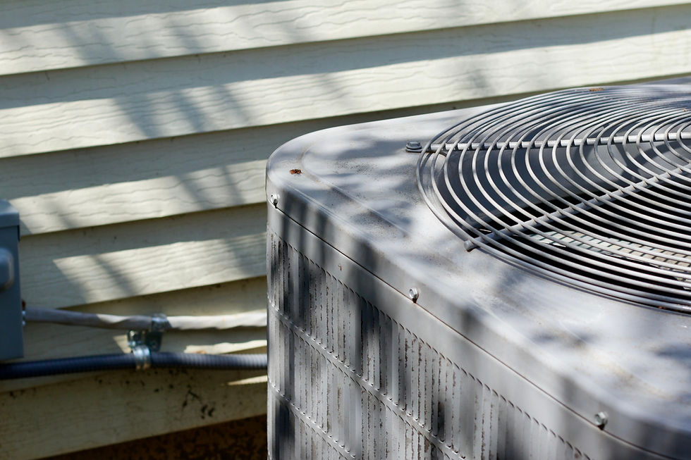 Outdoor air conditioning unit with metal grille in foreground, shadow patterns on beige siding background, sunny day, no visible text.