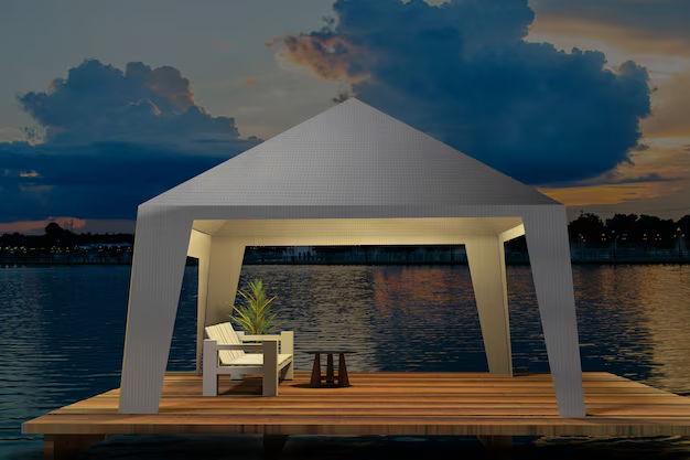 A modern gazebo with chairs and a plant is on a wooden dock by a calm lake during sunset, with dramatic clouds and reflections.