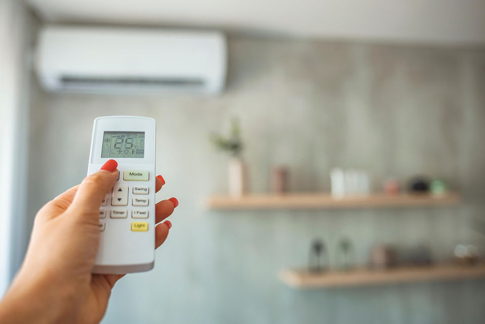 Hand holding a remote set to 26°C in a room with a wall-mounted air conditioner and blurred shelves. Mood is relaxed and cool.