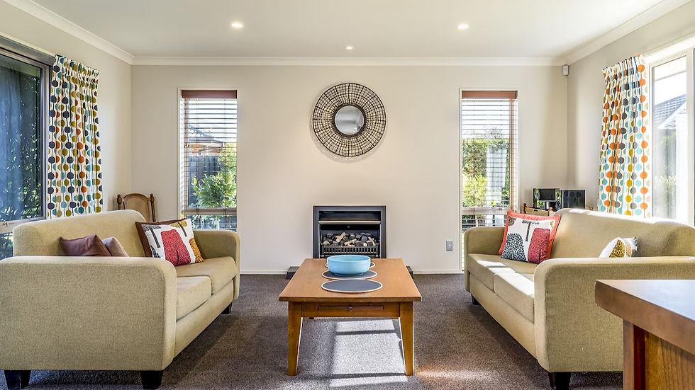 Cozy living room with beige sofas, colorful cushions, and a wooden coffee table. Circular mirror above a fireplace, vibrant polka-dot curtains.