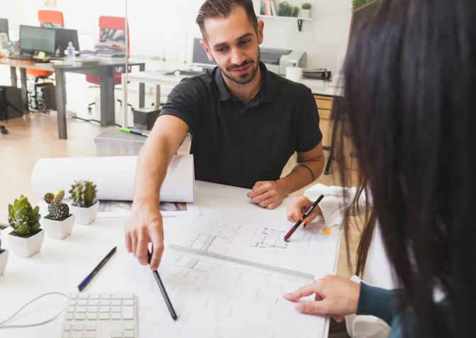 Man and woman discuss architectural plans at a desk with plants and office supplies. Bright office setting, collaborative mood.