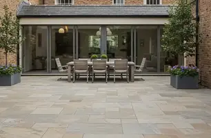 A modern patio with a wooden dining set and plants in large pots. Brick walls and large glass doors form the backdrop. Peaceful ambiance.