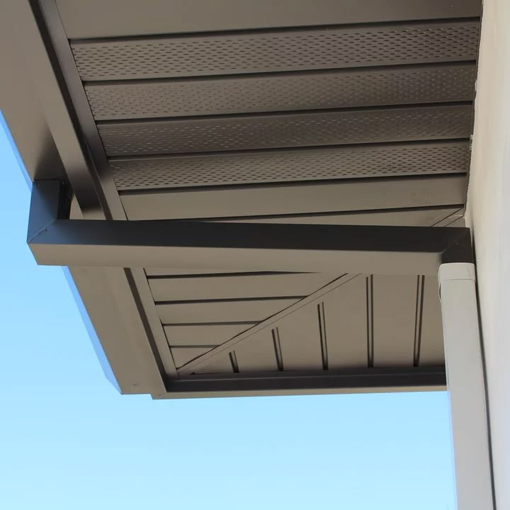 View of a brown roof eave with a gutter against a clear blue sky. The eave features perforated panels and smooth lines, creating a sleek look.