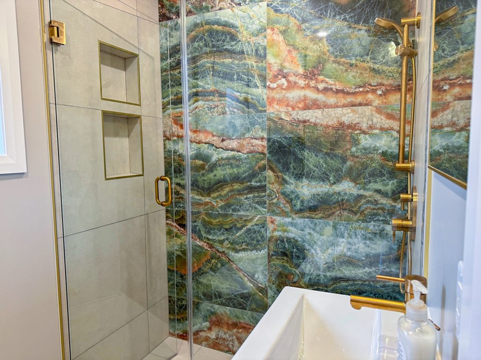 Shower with glass door, gold trim, and colorful stone wall. White sink with soap dispenser in foreground. Modern, elegant bathroom.
