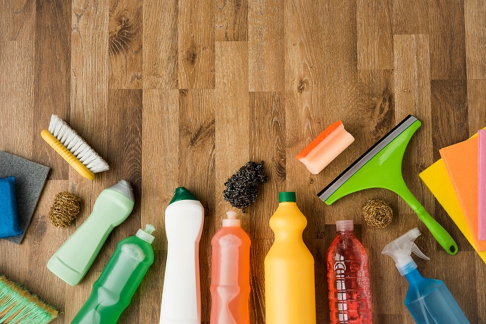 Cleaning supplies on wooden floor: colorful bottles, brushes, sponges, squeegee. Items neatly arranged, creating an organized appearance.