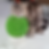 Cat rubbing face on green, textured ball resembling a cupcake in a room. Gray fur with stripes. Calm expression, scattered specks on floor.
