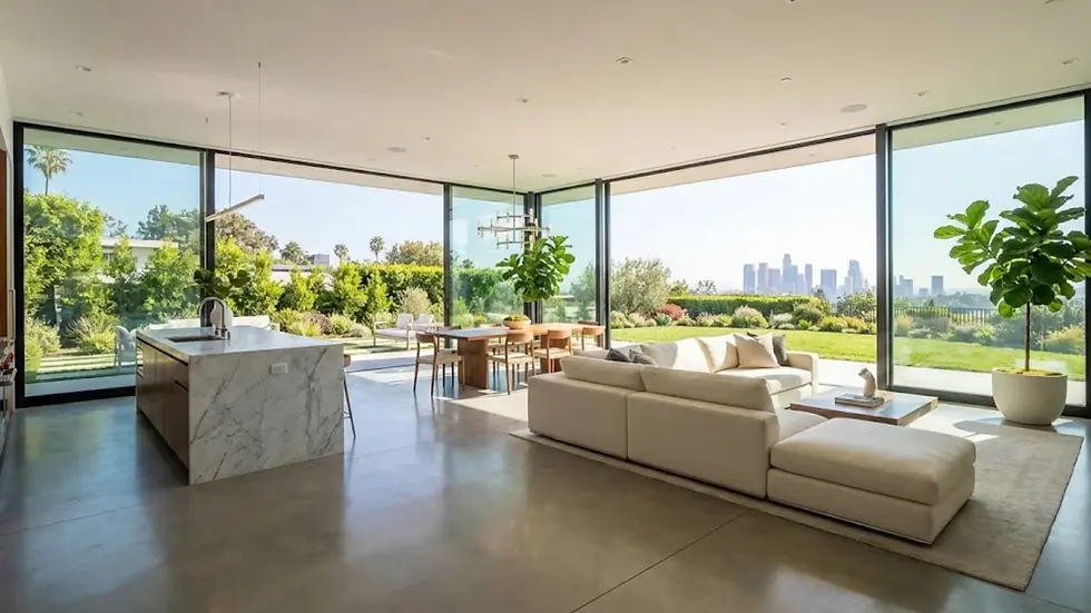 Modern living area with marble kitchen island, beige sofa, and dining table. Glass walls reveal a green garden and city skyline. Bright, airy mood.