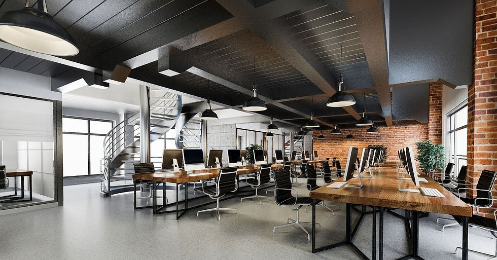 Modern office with long wooden desks and computers, black chairs, brick walls, spiral staircase, large windows, and industrial lighting.