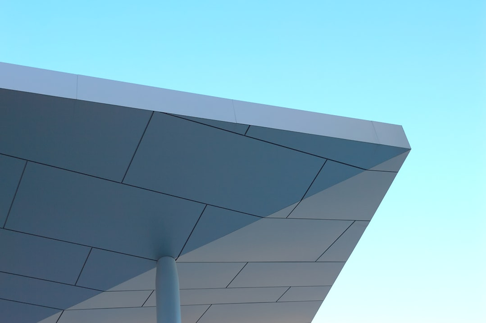 Angled view of a modern, geometric roof structure with a light blue sky background. The panels are sleek and metallic.