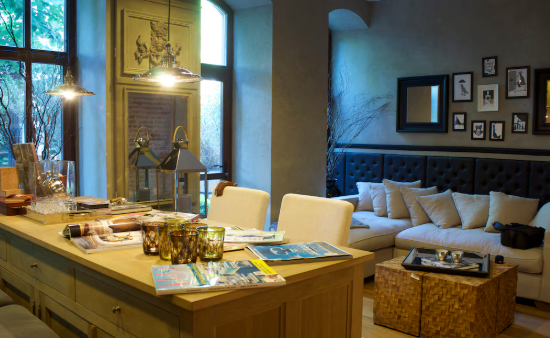 Cozy living room with tan sofa, wooden coffee table, and kitchen island. Magazines and glasses on the island, soft lighting, framed photos.
