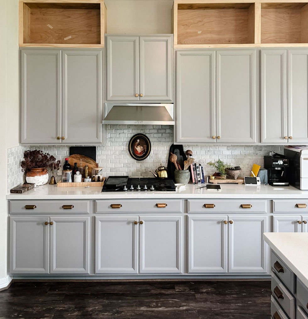 Modern kitchen with gray cabinetry and white countertops. Backsplash with small tiles, cooking utensils, plants, and a coffee maker on display.