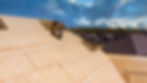 Worker on roof installs wooden panels, secured by rope. Background shows suburban houses and cloudy sky. Mood is industrious.