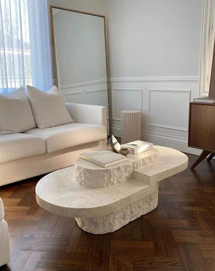 Beige sofa and stone coffee table with books create a cozy, modern living room. Large mirror, parquet floor, and soft light enhance calmness.