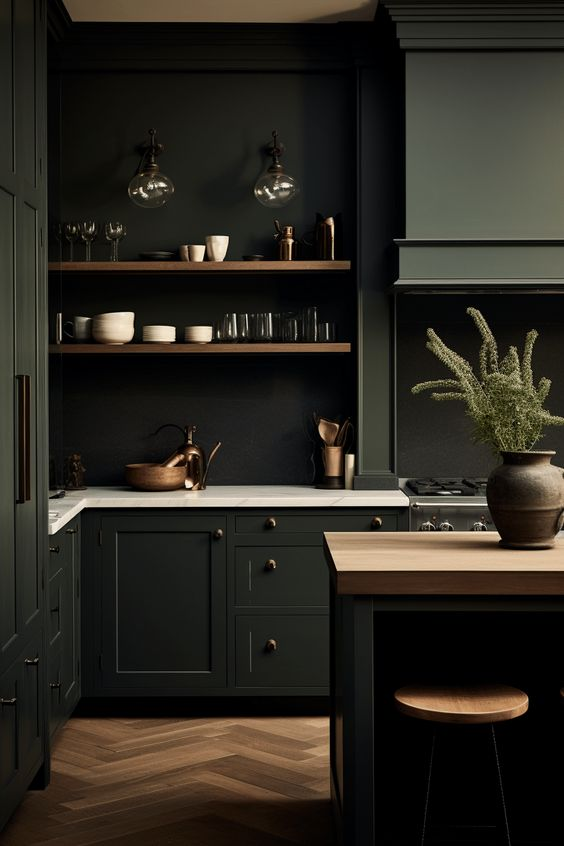Elegant kitchen with dark cabinetry and brass accents. The design features open wooden shelving, marble countertops, and warm copper decor. A small kitchen island with a wooden top adds functionality, while glass pendant lights and a herringbone floor pattern bring sophistication and warmth to the cozy, modern space.