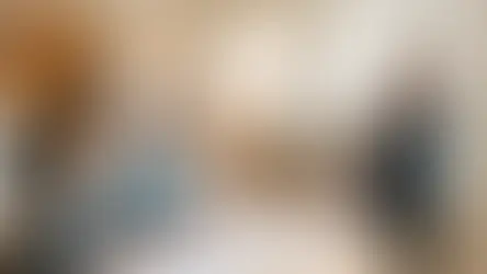 A woman in black presents to a seated couple reviewing blueprints in a bright, modern living room with wooden decor, conveying a professional mood.