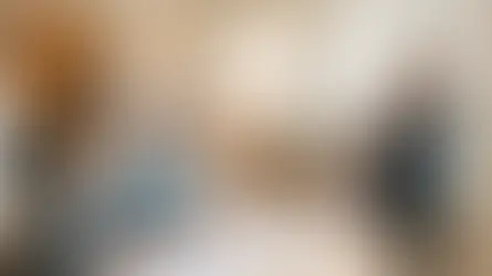 A woman in black presents to a seated couple reviewing blueprints in a bright, modern living room with wooden decor, conveying a professional mood.