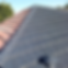 Roof with half red tiles, half painted gray, under clear sky. Trees in background. Contrast highlights transformation or renovation.