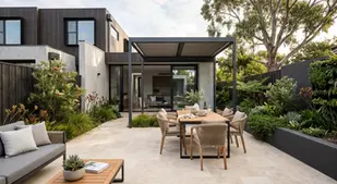 Modern patio with a wooden dining set under a pergola, surrounded by lush greenery. A sleek house and large tree create a serene ambiance.