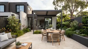 Modern patio with a wooden dining set under a pergola, surrounded by lush greenery. A sleek house and large tree create a serene ambiance.