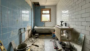 Renovation in progress in a bathroom with blue and white tiled walls, tools scattered, and a window. Mood is industrious and messy.