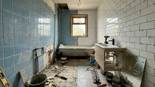 Renovation in progress in a bathroom with blue and white tiled walls, tools scattered, and a window. Mood is industrious and messy.