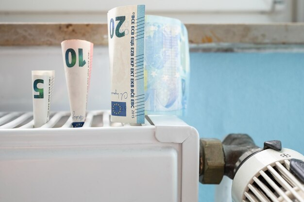 Euro banknotes are placed on a white radiator with a blue wall in the background, suggesting heating cost concerns.