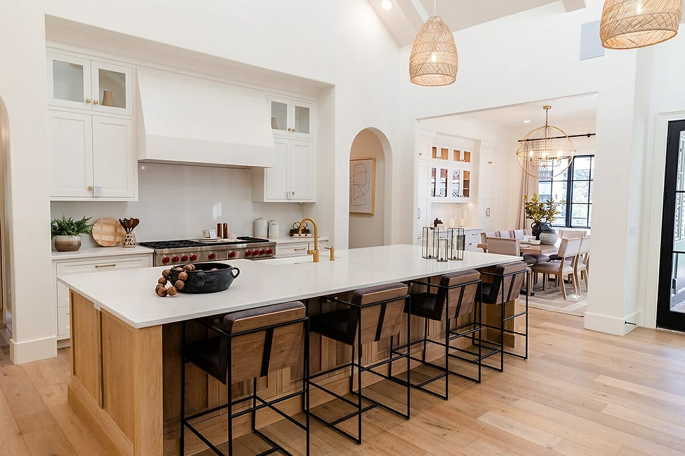 Modern kitchen with white cabinets, large island with bar stools, pendant lights, and dining area. Bright and spacious with wood accents.