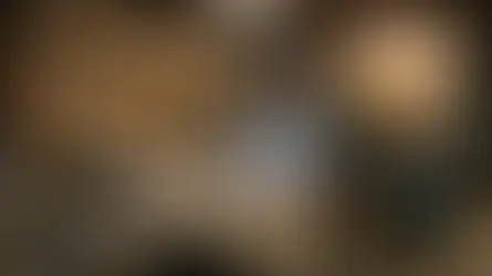 Worker welding metal in a workshop, surrounded by tools on shelves. Sparks fly as bright light illuminates the scene, conveying focus.