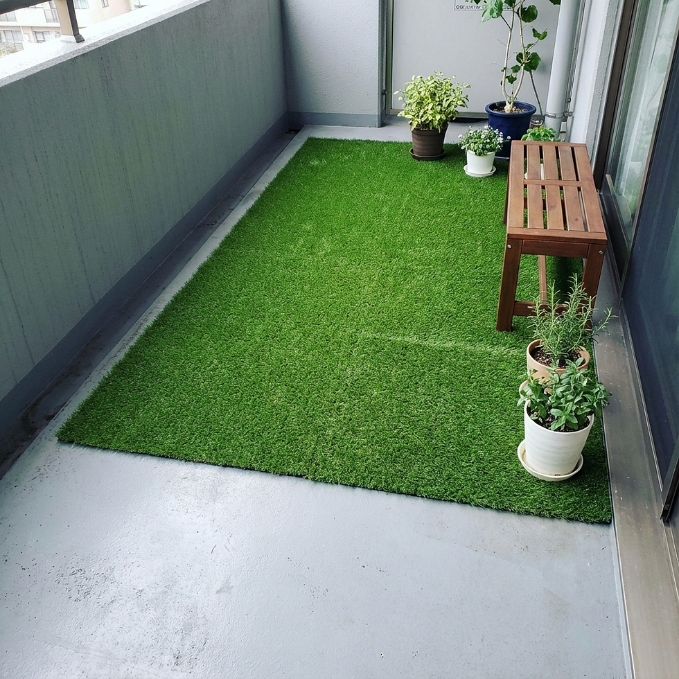 Small balcony with green artificial turf, wooden bench, and potted plants. Neutral walls and a calm, tidy atmosphere.