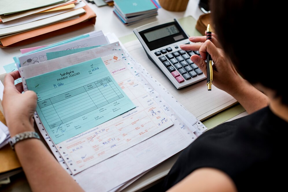 Person holding a blue payment voucher, using a calculator on a desk with paperwork. Pens and folders in the background. Work focus mood.