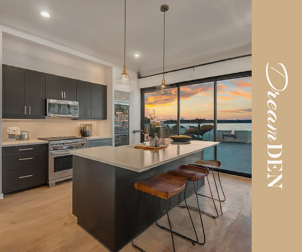 Modern kitchen featuring a large island with barstools, dark cabinetry, stainless steel appliances, and expansive floor-to-ceiling windows offering a stunning sunset view over a body of water. The space is styled with DreamDen branding.