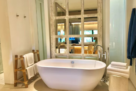 Luxurious bathroom with a white freestanding tub, large mirrored wall, and plush towels. Warm lighting and a blue towel on a door add elegance.