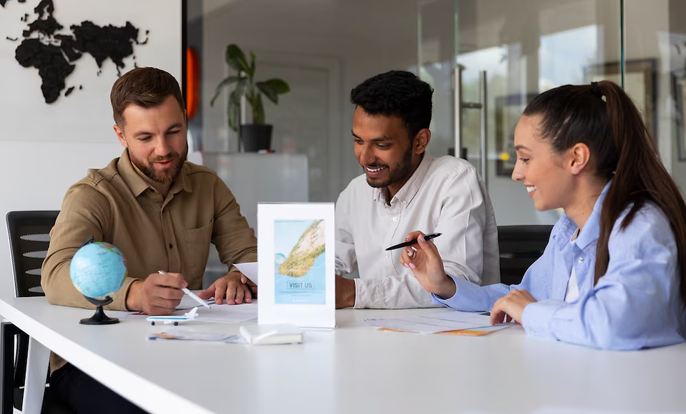 Three people sit at a table, collaborating over documents. A small globe and a "Visit Us" sign are on the table. They appear cheerful.