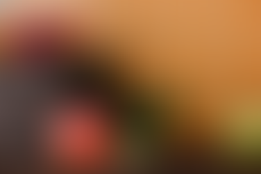 Basket with red and green apples on a wooden table, one apple with a bite. Orange tiled background, leafy greens beside.