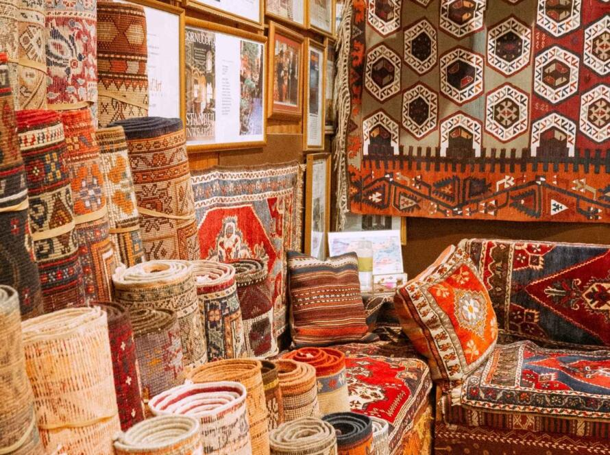 Rolled and displayed colorful Persian rugs in a cozy store, with intricate patterns and framed art on the walls, creating a vibrant ambiance.
