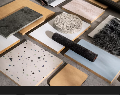 Assorted material samples on a table, including wood, stone, terrazzo, and faux fur, arranged in a grid. Neutral tones and varied textures.
