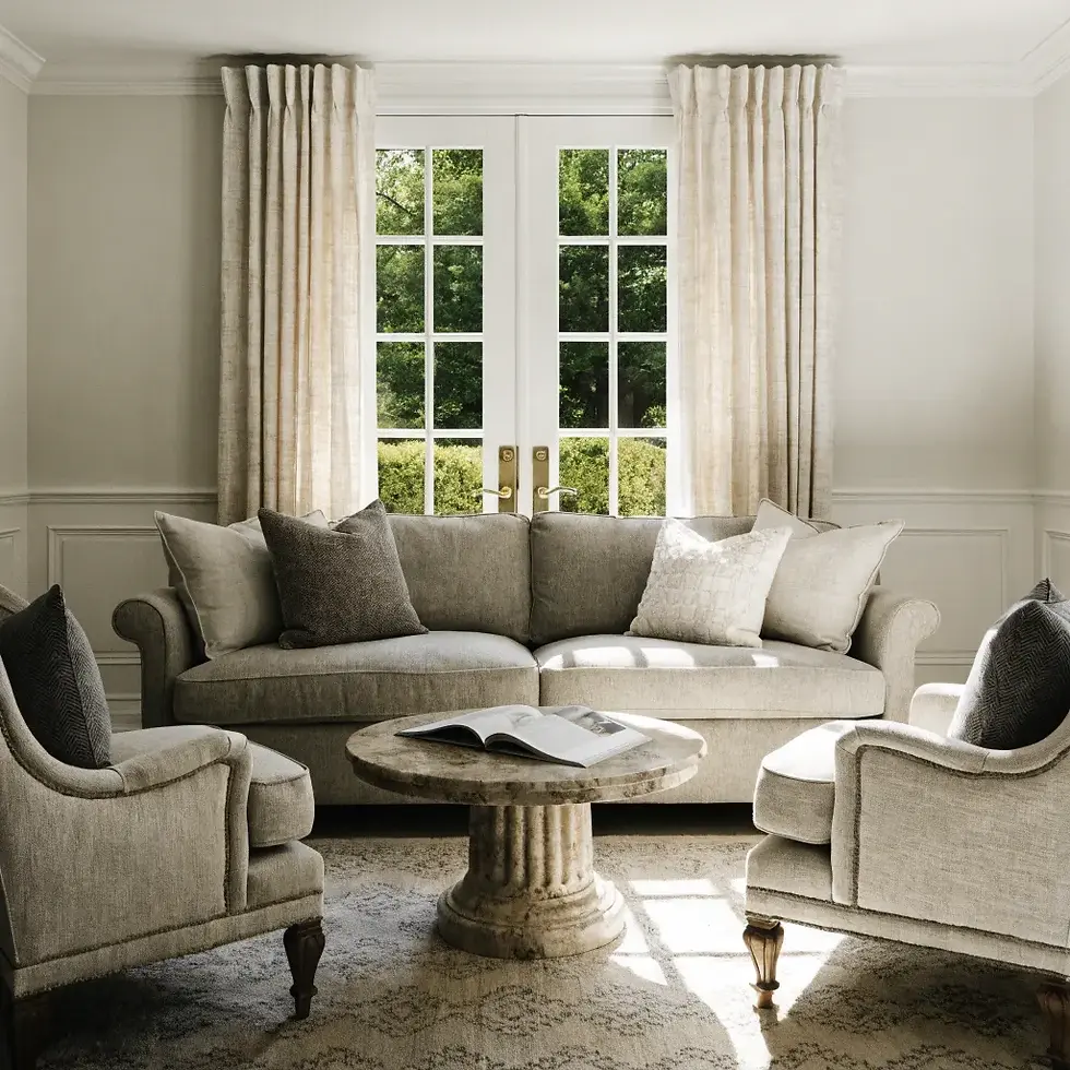 Elegant living room with beige sofa, two armchairs, and a round marble coffee table. Sunlight streams through glass doors with garden view.