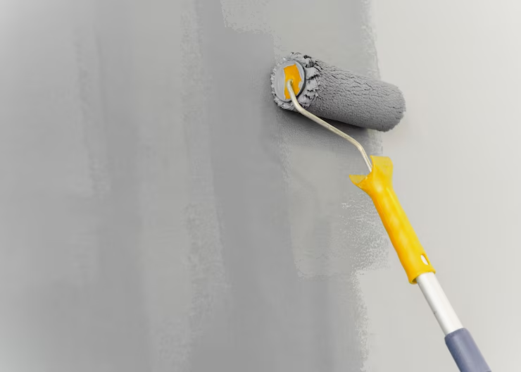 Paint roller with a yellow handle applying grey paint to a wall. The wall shows fresh strokes, giving a smooth, clean appearance.