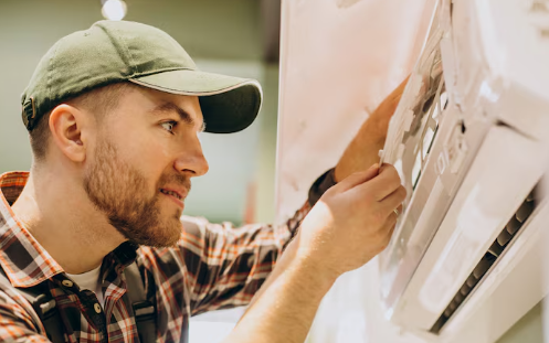 Man in a green cap and plaid shirt fixes an air conditioner. Focused expression, indoor setting with soft lighting.