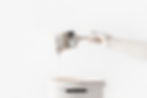 A hand holding a paintbrush dripping with white paint above a matching paint bucket. Minimalist white background, conveying a clean mood.