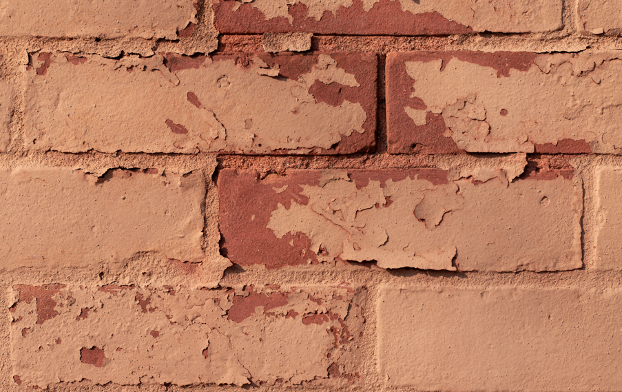 Close-up of a red brick wall with peeling beige paint, showing texture and weathered appearance. No visible text or additional elements.