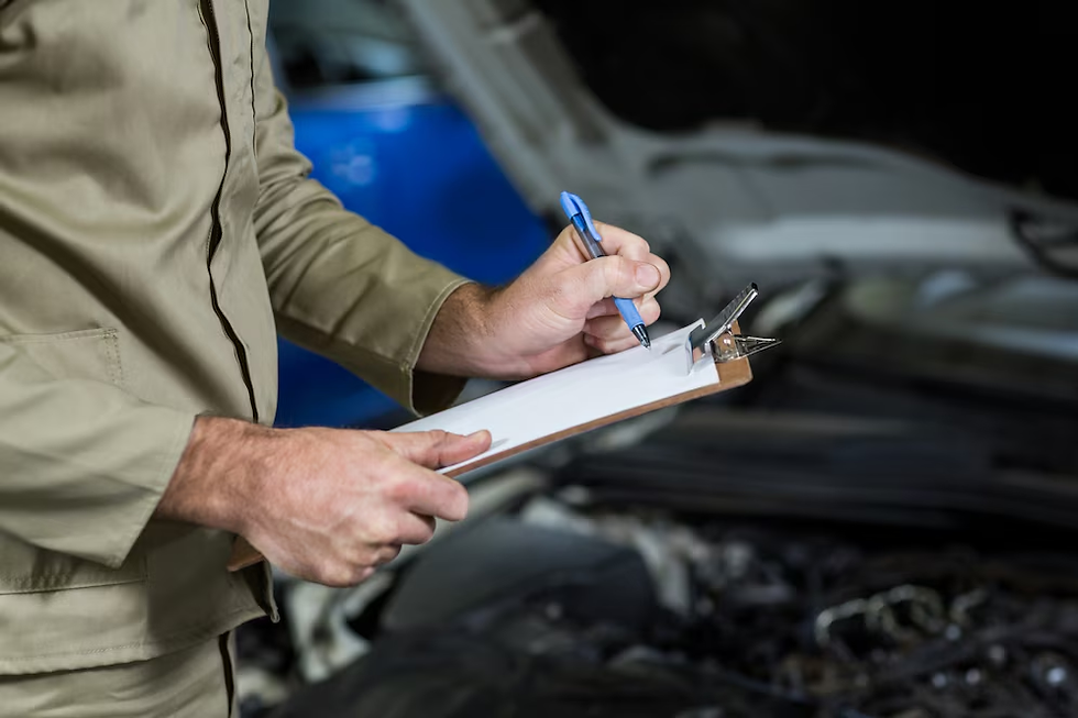 Mechanic in beige uniform writes on clipboard near open car hood. Background shows a blue car. Hands-on, focused atmosphere.