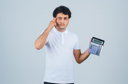 Man in a white shirt holds a calculator and points to his temple thoughtfully. Plain light gray background, focused expression.